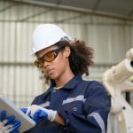 A young female worker is controlling a mechanical robot.